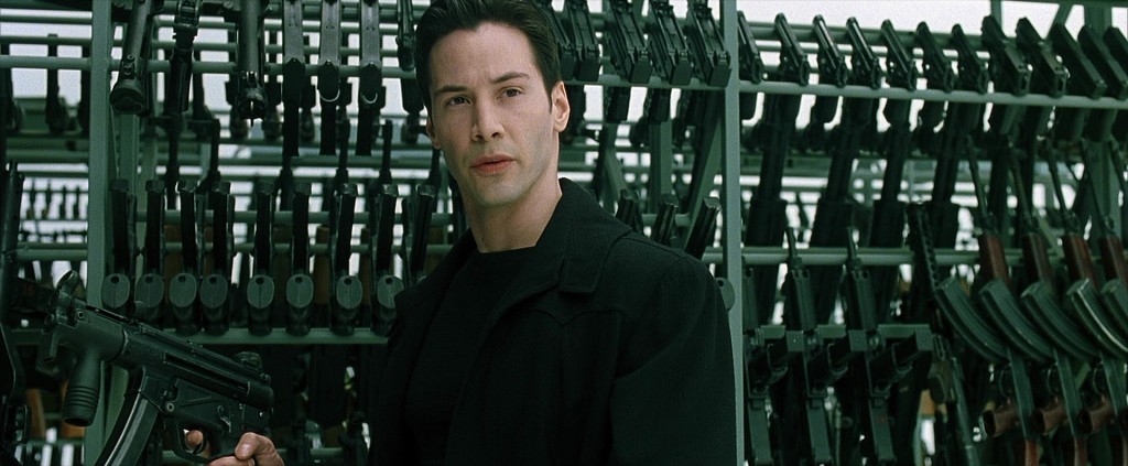 Keanu Reeves as Neo in the matrix: standing next to a large inventory of weapons for the final action scene in the movie.