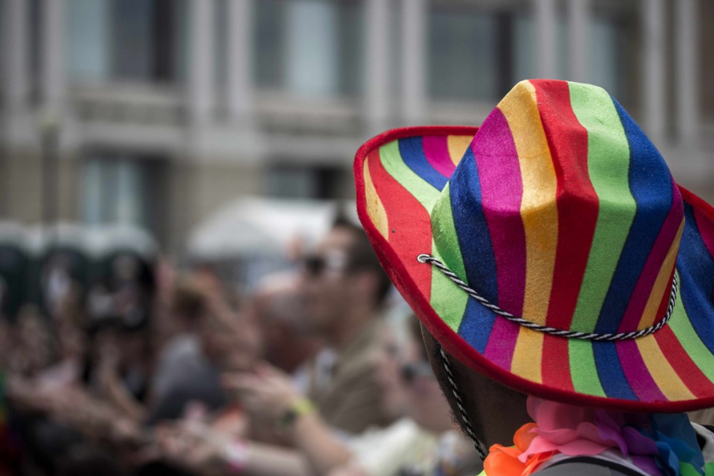 Guy with a rainbow cowboy hat glances into the crowd. 